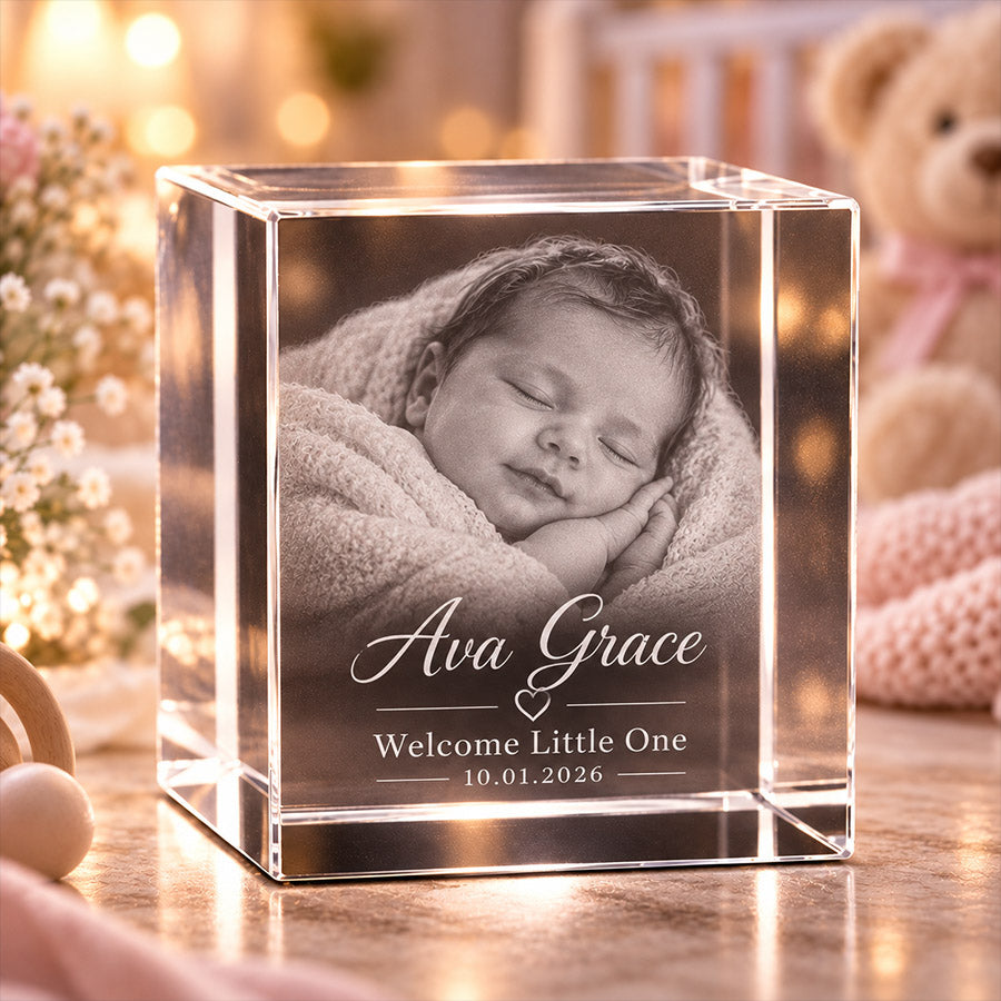 Personalized crystal photo block featuring a sleeping newborn baby portrait with engraved text "Ava Grace", "Welcome Little One", and date "10.01.2026" in a soft pink nursery setting -- lxi-context:for-baby -- lxi-context:new-baby