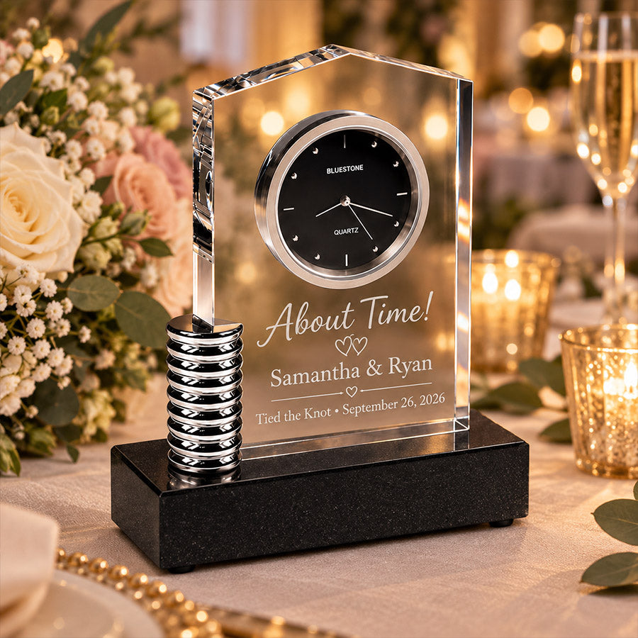 Crystal desk clock award with wedding engraving reading About Time!, Samantha & Ryan, and Tied the Knot • September 26, 2026 displayed in an elegant candlelit wedding reception setting with blush florals and champagne glasses -- lxi-context:wedding