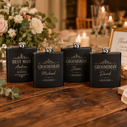 Set of four engraved black matte stainless steel flasks on a rustic wood table, including one Best Man flask for Andrew and three Groomsman flasks for Michael, Jason, and David, styled in a warm wedding setting with candles and floral décor. -- lxi-context:wedding