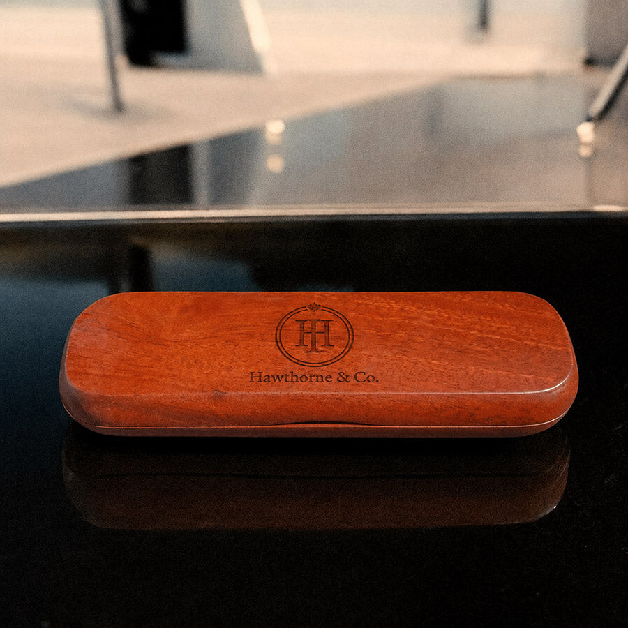 Personalized rosewood pen box with engraved Hawthorne & Co. logo shown closed on a dark reflective tabletop