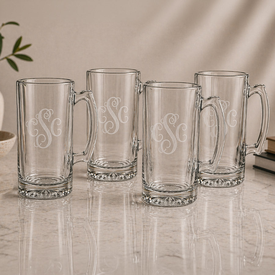 Set of four personalized clear glass beer mugs with matching engraved three letter monograms on a neutral tabletop display