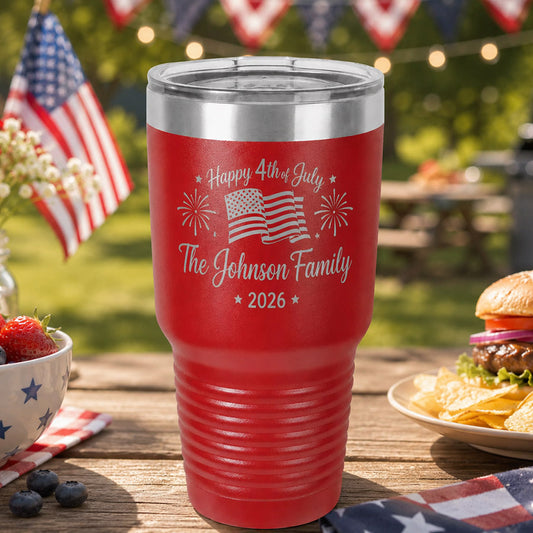 Red insulated engraved tumbler with “Happy 4th of July The Johnson Family 2026” design, shown outdoors on a patriotic picnic table with flags, fireworks motifs, berries, and a burger -- lxi-context:4th-of-july