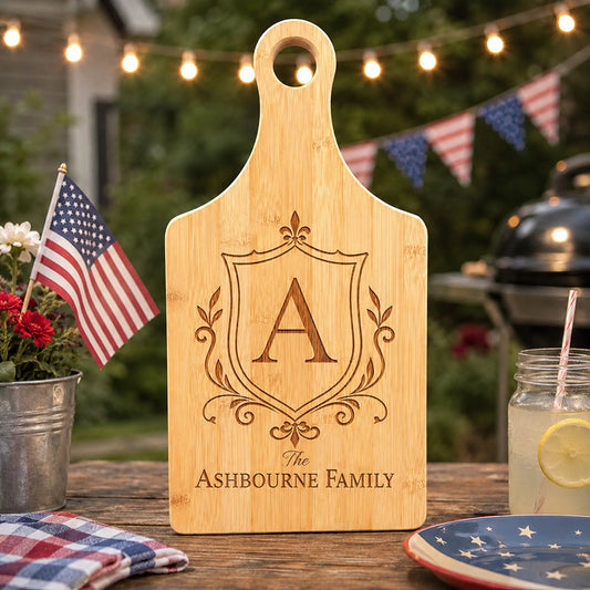 Personalized bamboo cutting board with engraved Ashbourne Family crest, shown on a patriotic 4th of July outdoor table -- lxi-context:4th-of-july