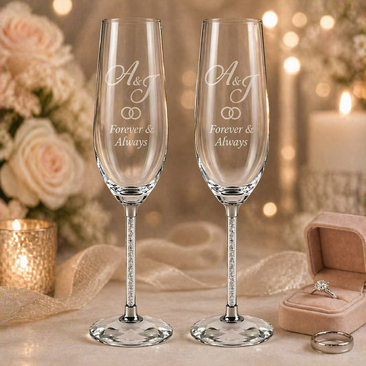 Pair of engraved wedding champagne flutes with initials "A&T" and "Forever & Always" beside a ring box and wedding bands -- lxi-context:wedding